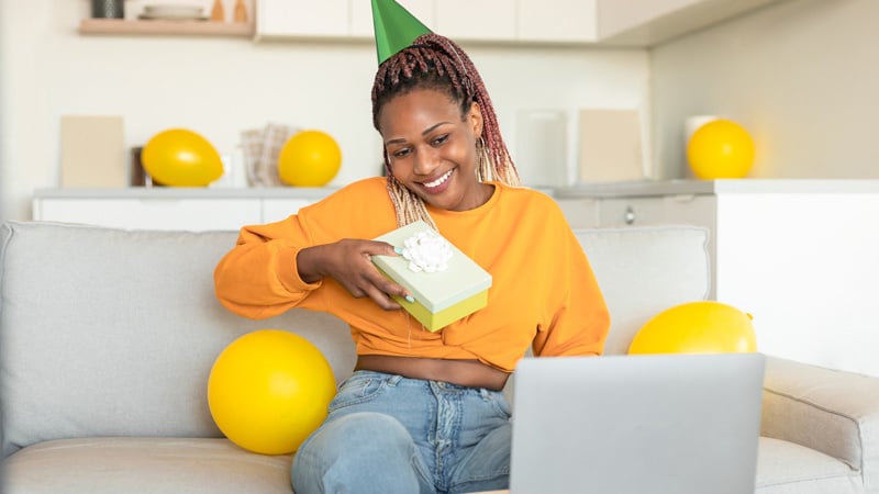 happy-african-american-lady-looking-laptop-receiving-gift-from-friends-celebrating-bday-via-video-call-home